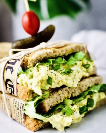 egg salad sandwich wrapped in paper with pickle and tomato on top