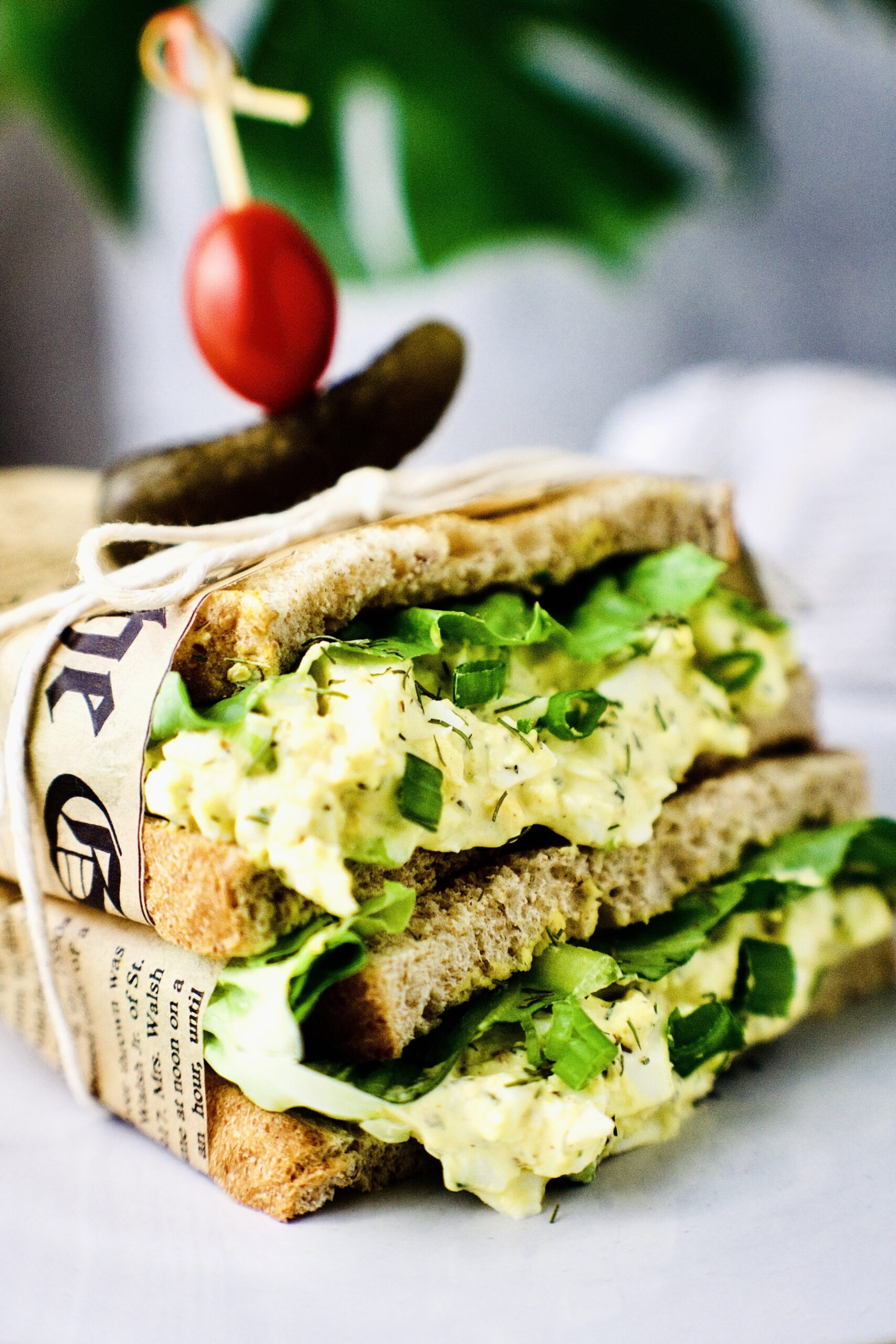 egg salad sandwich wrapped in paper with pickle and tomato on top