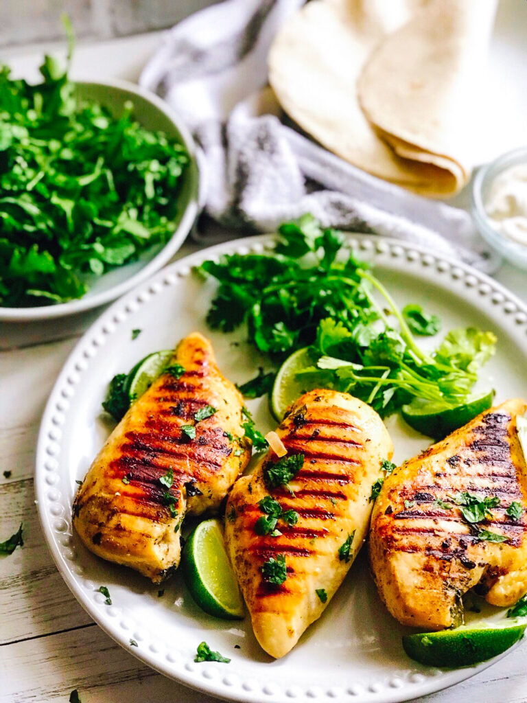 Reverse Seared Tequila Lime Chicken Breasts | Keto, Low-Carb, on a white platewith tortillas and arugula pictured in the background.