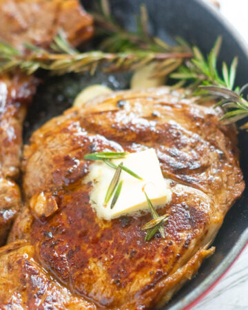 pan seared boneless ribeye with butter and herbs in a cast iron skillet