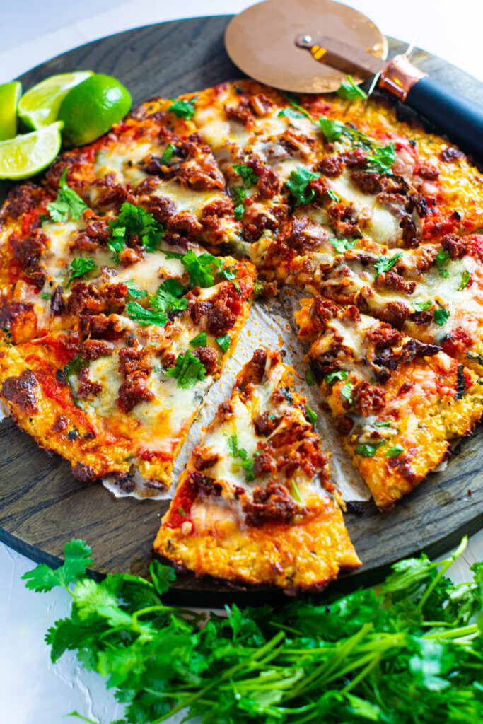 keto-friendly chorizo lime pizza on a brown cutting board with pizza roller