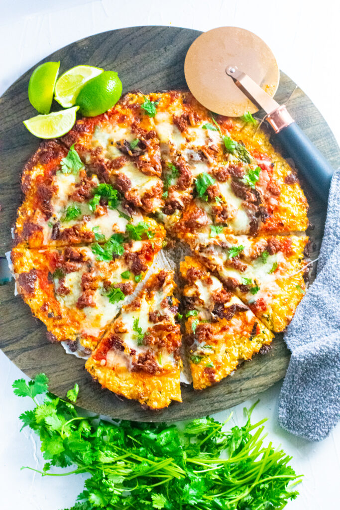 keto-friendly chorizo lime pizza on a brown cutting board with pizza roller