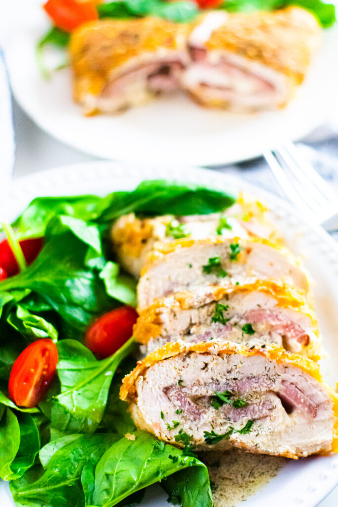 Sliced Chicken Cordon Bleu with salad on white plate