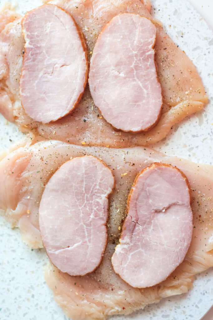 raw chicken breasts covered in ham slices
