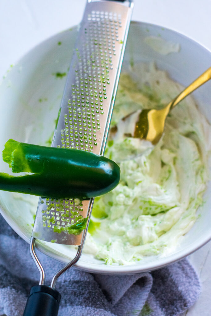 jalapeno being zested into a cream cheese mixture
