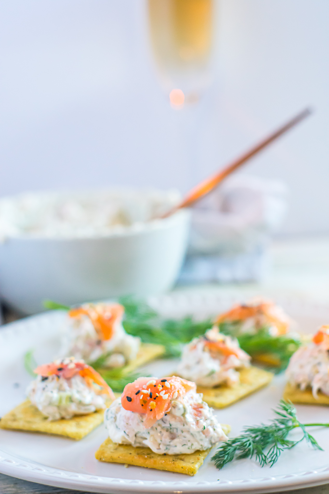 Smoked salmon dip with crackers on a white plate with dill garnishment.