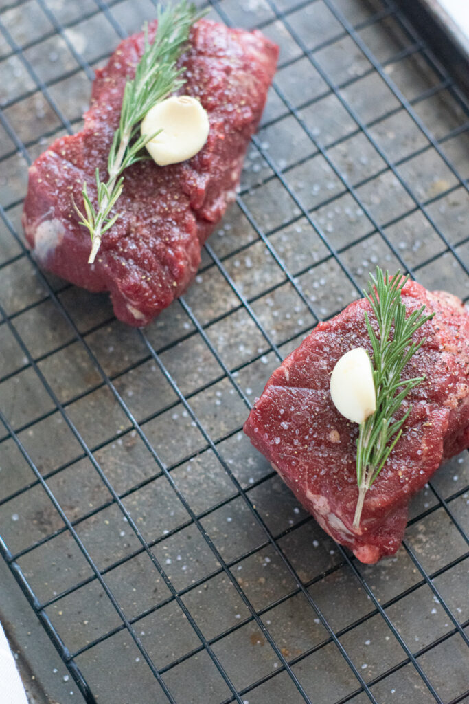 raw filet mignon topped with garlic and rosemary on a baking sheet.