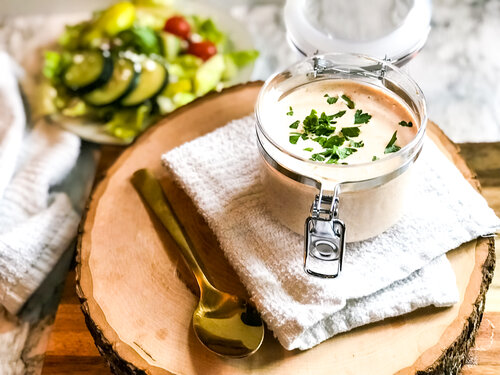 Blackened Ranch dressing in a glass container with salad in background.
