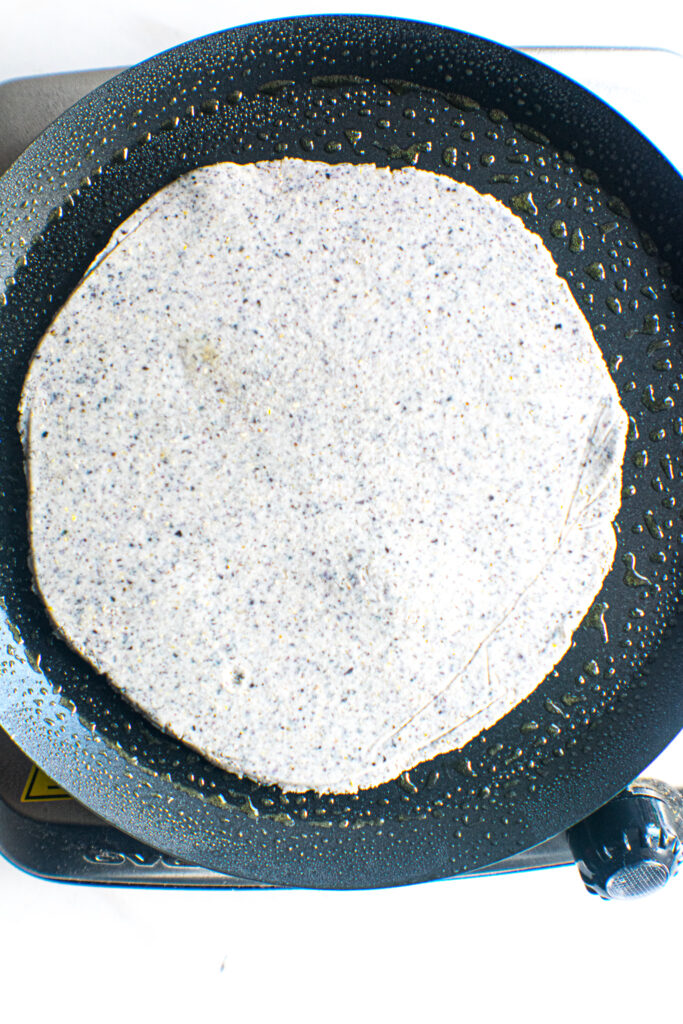 Carbon steel comal with metal handles cooking a blue corn tortilla