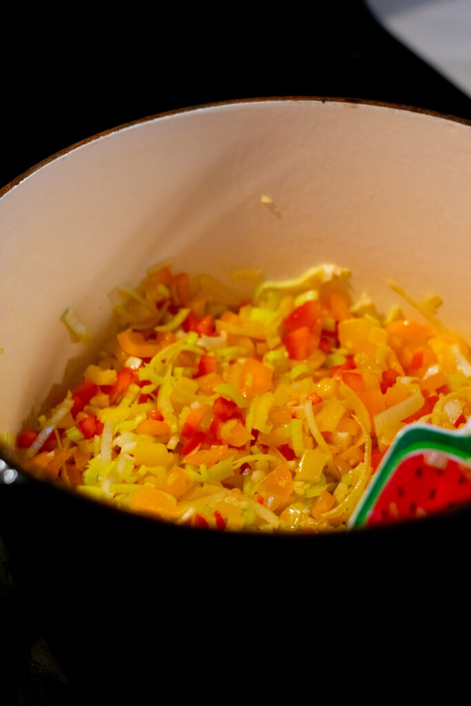 Diced vegetables cooking in a dutch oven for stuffed bell pepper soup.