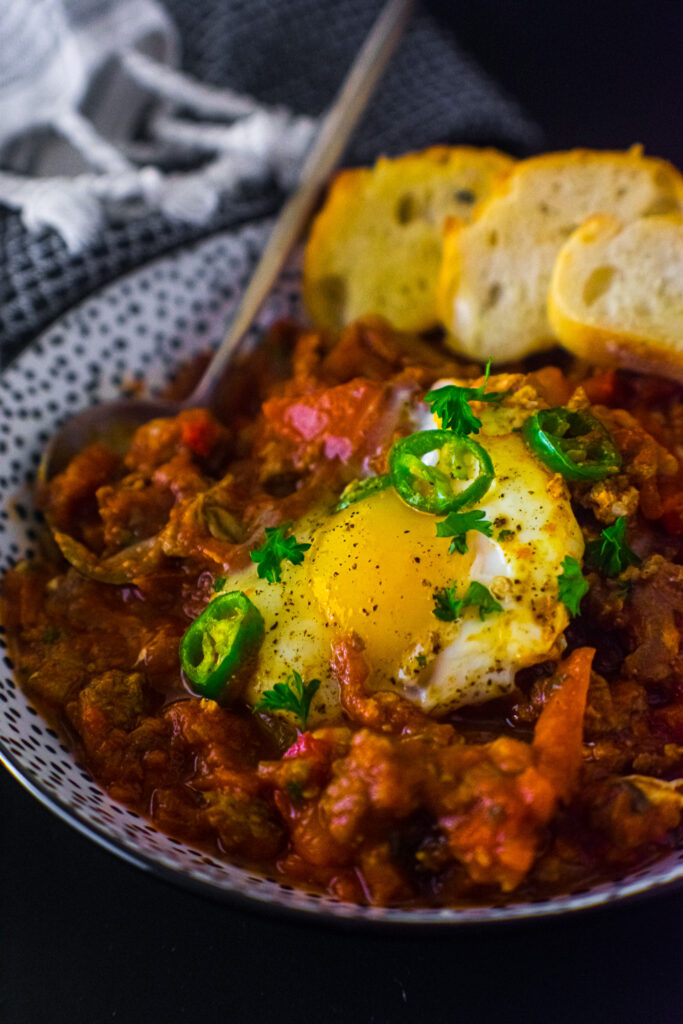 Shakshuka with turkey sausage in a small bowl with bread and spoon.