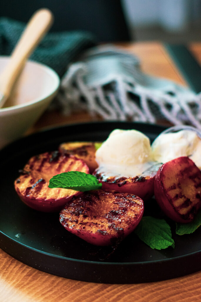 Grilled peaches and ice cream on a black plate.